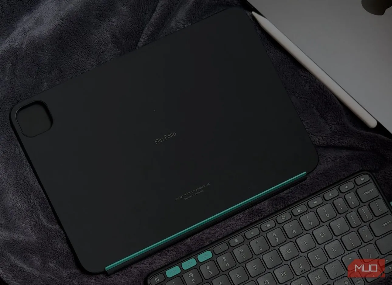Bàn phím Logitech Flip Folio đặt cạnh iPad trên chăn, cho thấy thiết kế nhỏ gọn và các phím tắt iPadOS chuyên dụng tiện lợi.