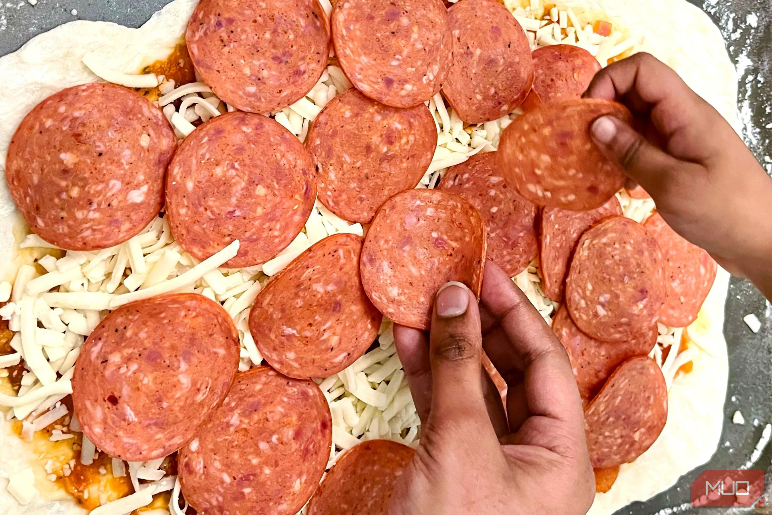 Bàn tay đang rắc phô mai lên chiếc pizza đang được làm dở, tạo cảm giác về quá trình chuẩn bị món ăn