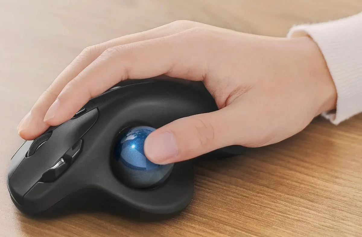 Bàn tay người dùng đang điều khiển chuột trackball dùng ngón cái, cho thấy tư thế tay thoải mái và tự nhiên.