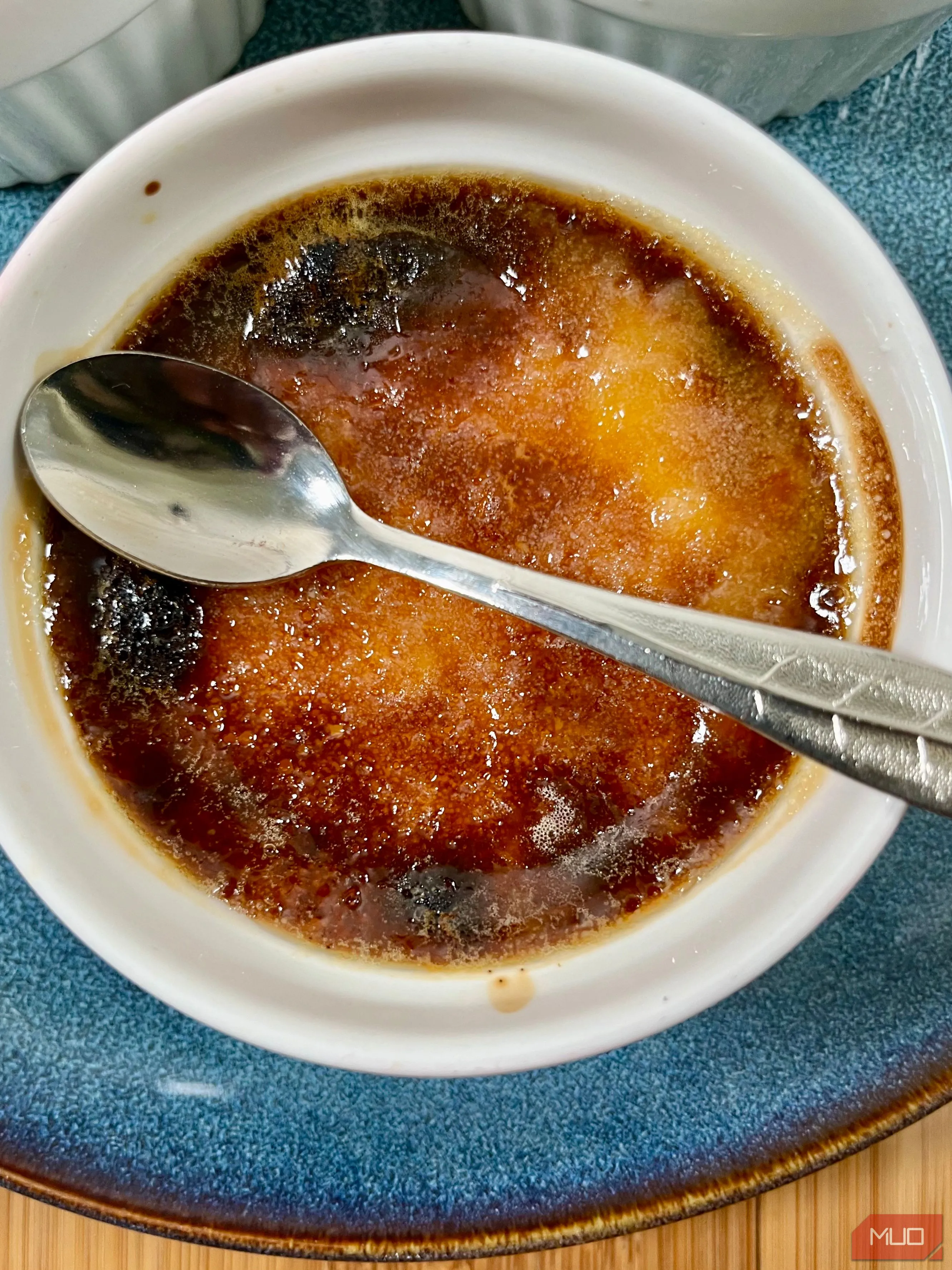 Bát kem Crème brûlée với lớp đường caramel cháy xém, đặt trên nền gỗ tối với ánh sáng từ một phía