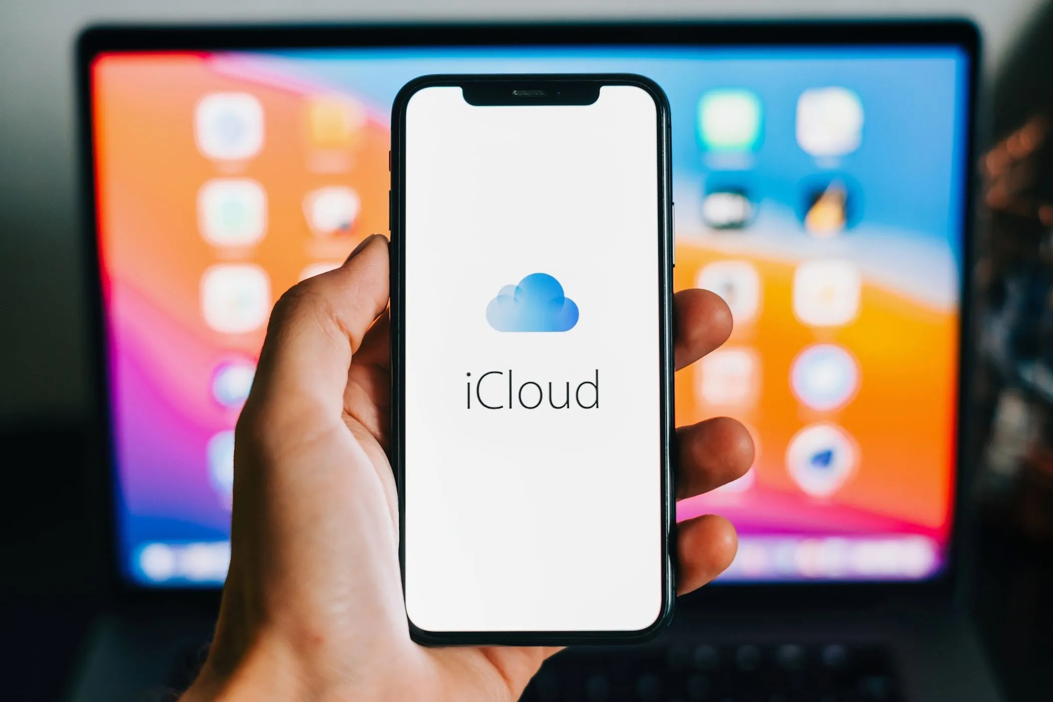 Biểu tượng iCloud hiển thị trên màn hình iPhone, phía sau là máy MacBook, minh họa tầm quan trọng của dịch vụ iCloud+.