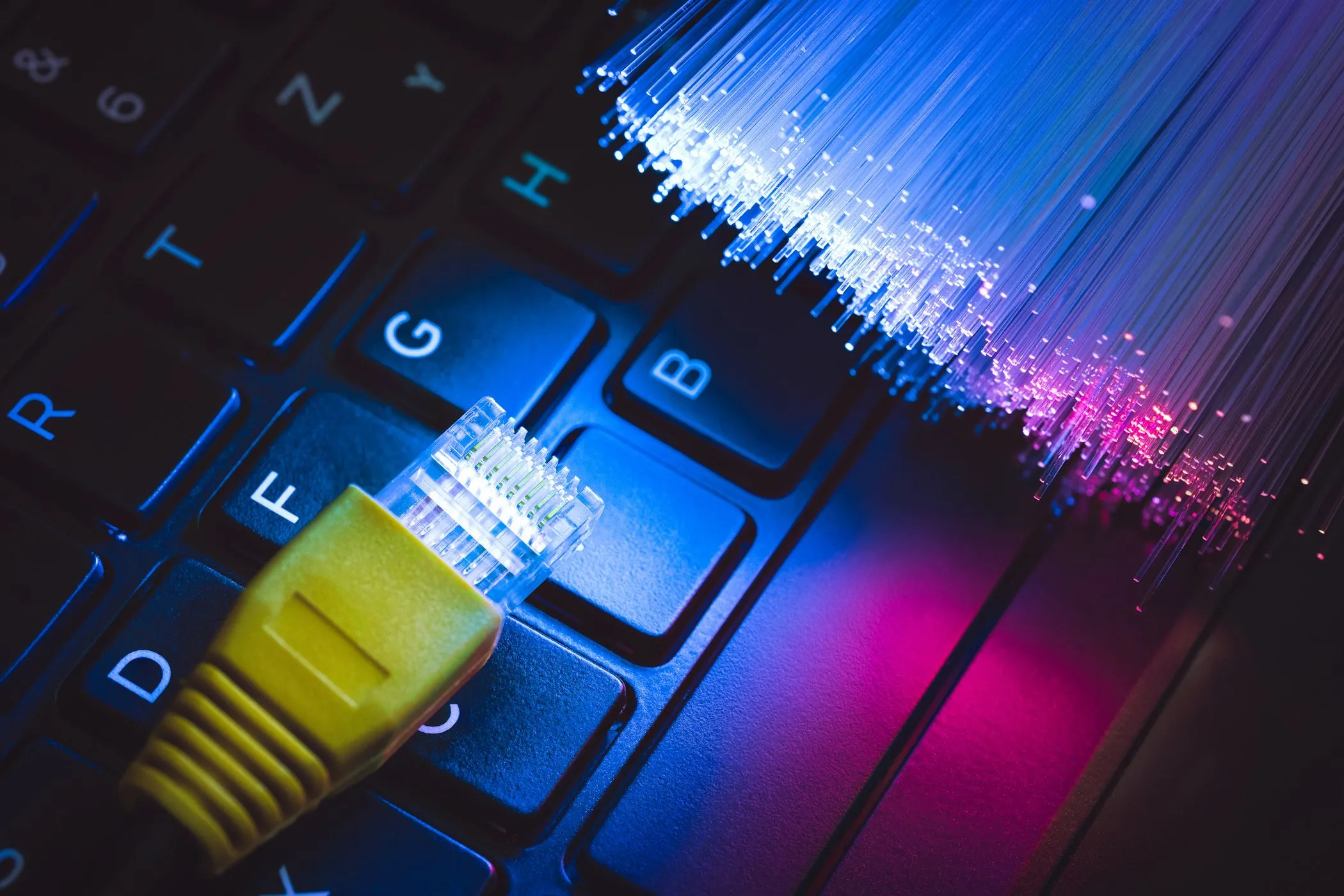 Cáp Ethernet và sợi quang trên bàn phím laptop, tượng trưng cho việc nâng cấp băng thông internet để có kết nối Wi-Fi ổn định hơn.