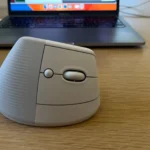Chuột không dây Logitech Lift bên cạnh máy tính xách tay trên bàn làm việc, thể hiện sự tiện lợi và gọn gàng.
