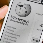 Điện thoại hiển thị ứng dụng Wikipedia đang mở, tượng trưng cho việc tra cứu thông tin và sự hỗ trợ của AI trong việc quản lý nội dung.