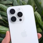 Điện thoại iPhone 16 Pro màu trắng trên tay người dùng, nổi bật trước nền cây xanh, minh họa thiết kế camera tinh tế.