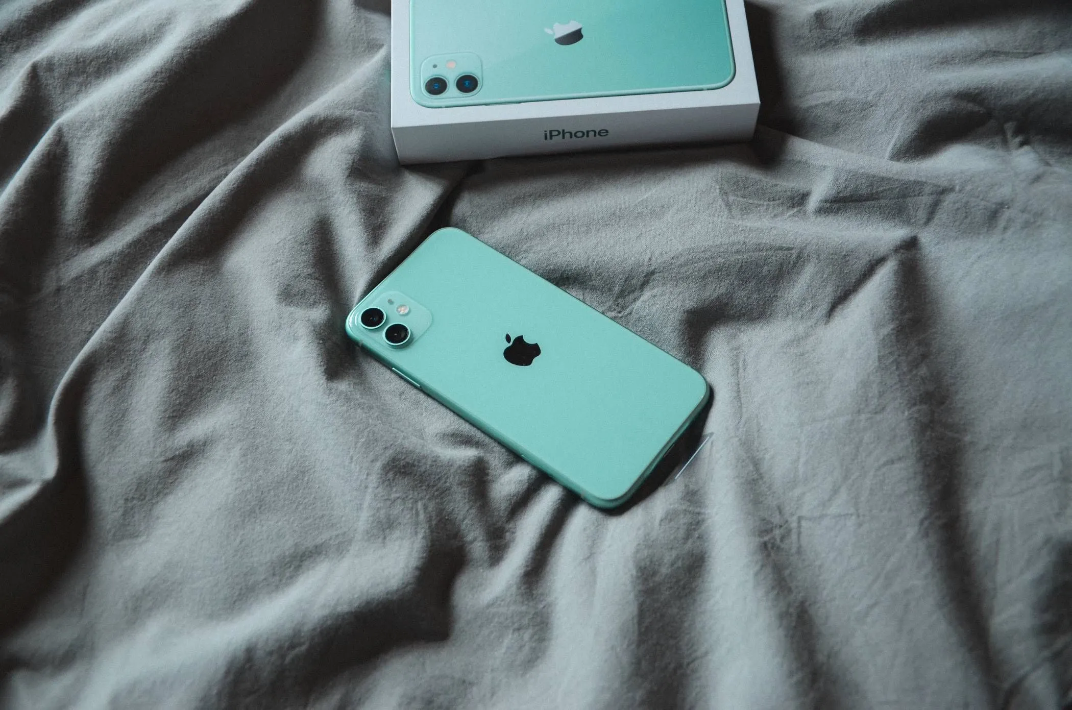 Điện thoại iPhone đặt trên chăn hoặc ga trải giường khi đang sạc, thể hiện rủi ro quá nhiệt khi sạc iPhone trên bề mặt mềm.