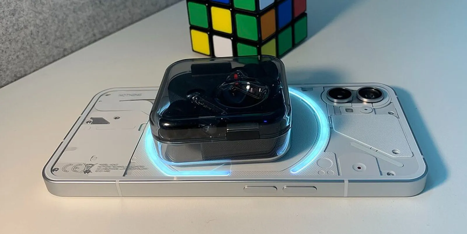 Điện thoại Nothing Phone (1) đang sạc không dây ngược cho tai nghe true wireless, đặt trên khối Rubik.