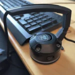 Giá đỡ dây chuột (mouse bungee) màu đen đặt trên bàn gỗ, giúp quản lý dây chuột gọn gàng.