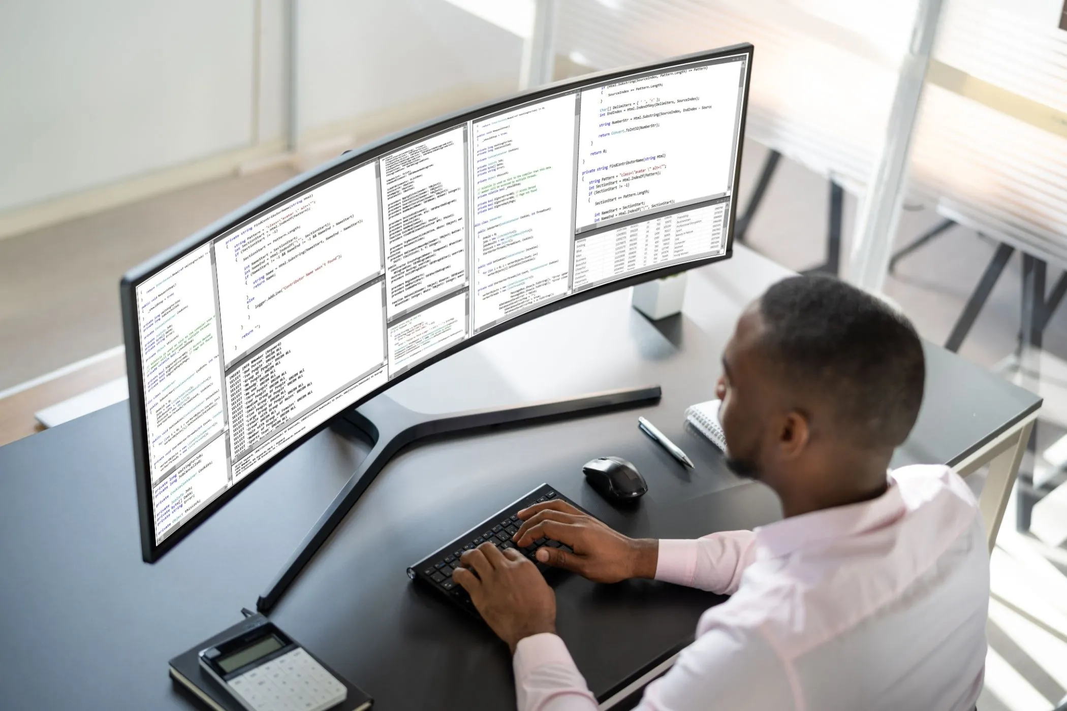 Màn hình ultrawide lớn trên bàn làm việc cùng người đàn ông đang gõ phím.