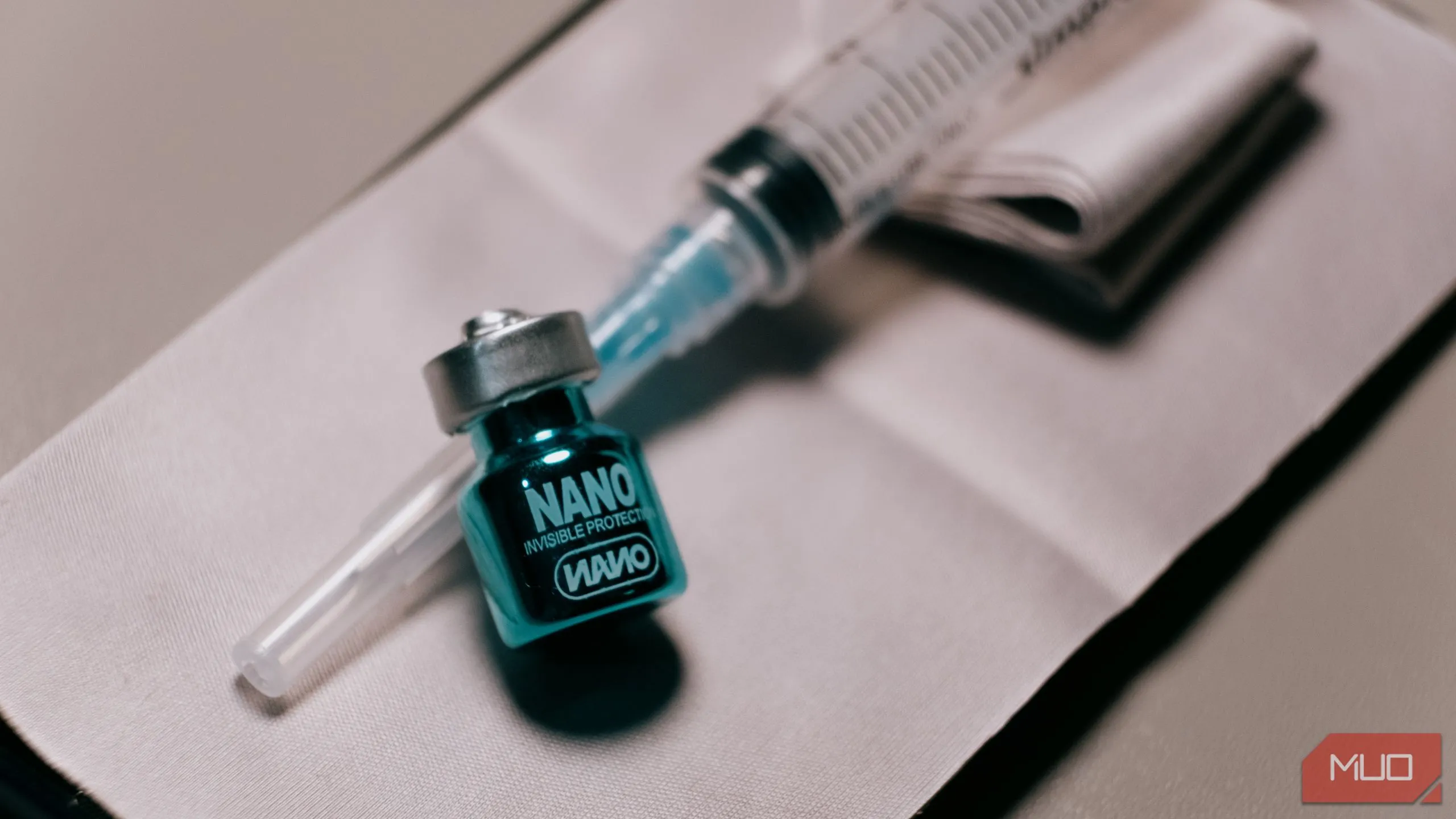 Một lọ dung dịch phủ nano oleophobic nhỏ đặt cạnh ống tiêm, minh họa cho việc chuẩn bị vật liệu thử nghiệm lớp phủ chống bám dầu.