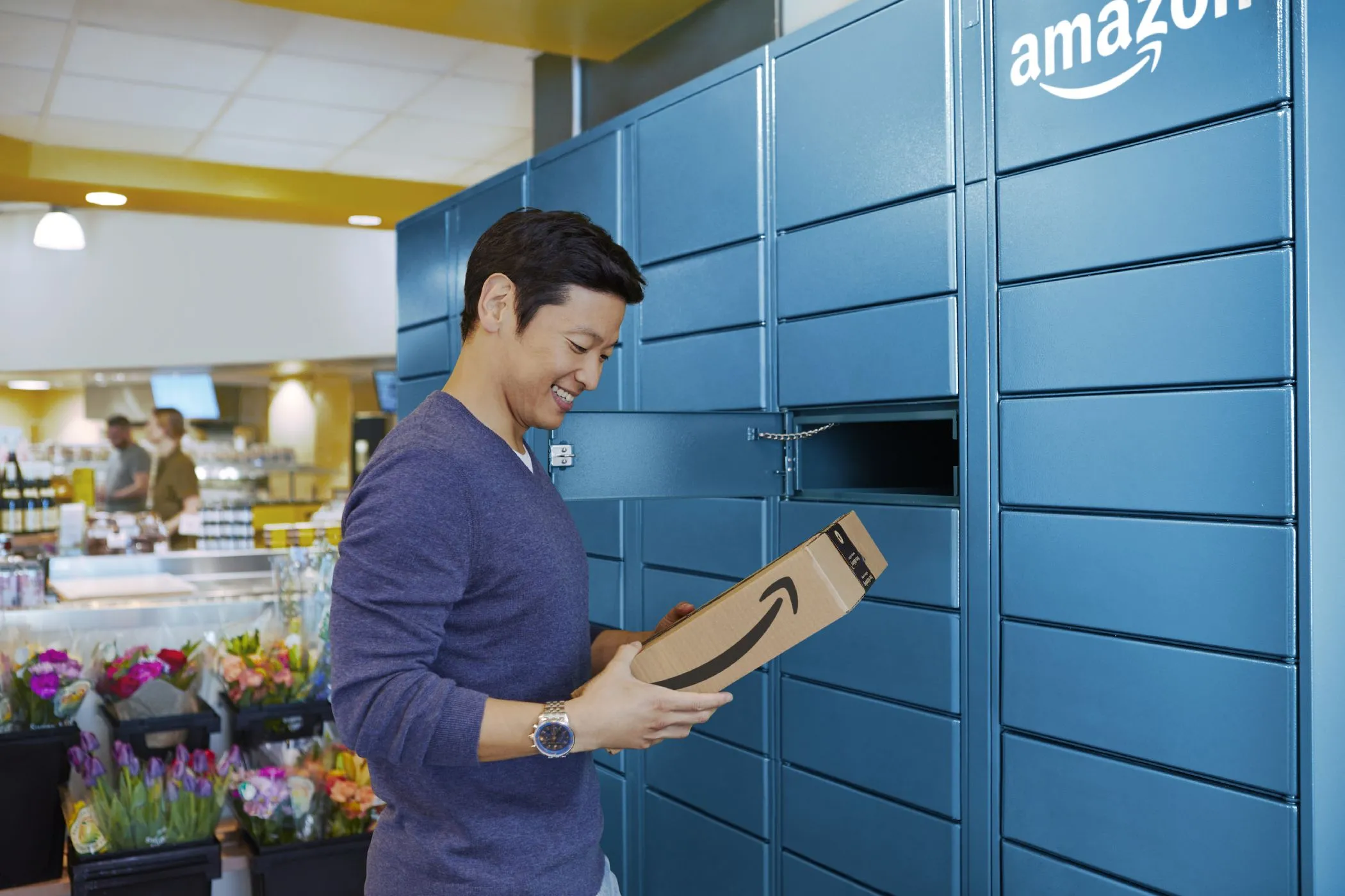 Một người đàn ông đang nhận gói hàng từ tủ khóa Amazon Locker, thể hiện phương pháp giao hàng ẩn danh để bảo vệ địa chỉ nhà riêng