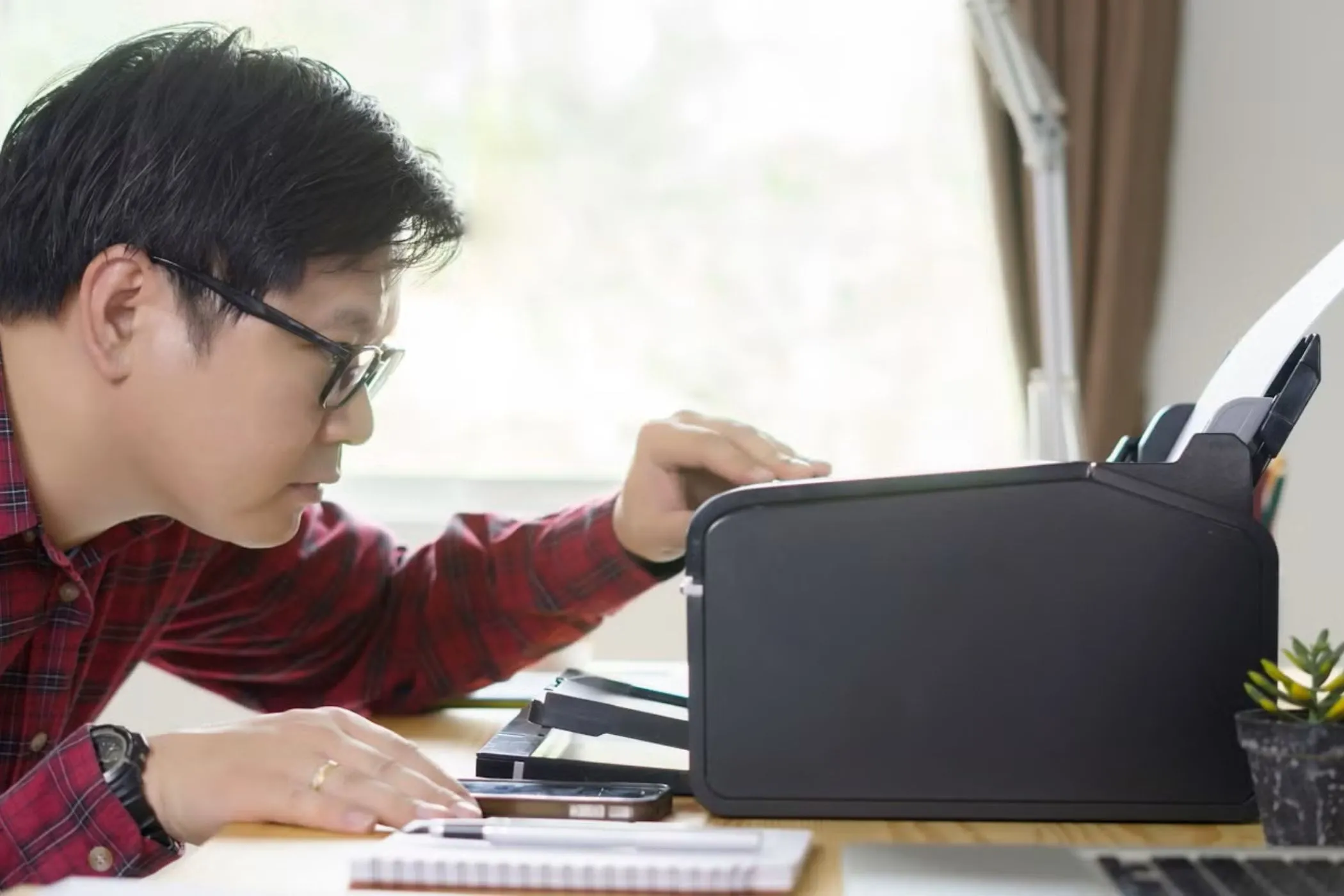 Một người đàn ông đang nhìn vào máy in trên bàn làm việc, tượng trưng cho những vấn đề tương thích khi kết nối thiết bị ngoại vi với Chromebook.