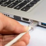 Người đàn ông cắm cáp Ethernet vào laptop Windows, biểu tượng cho kết nối mạng an toàn và trực tiếp.