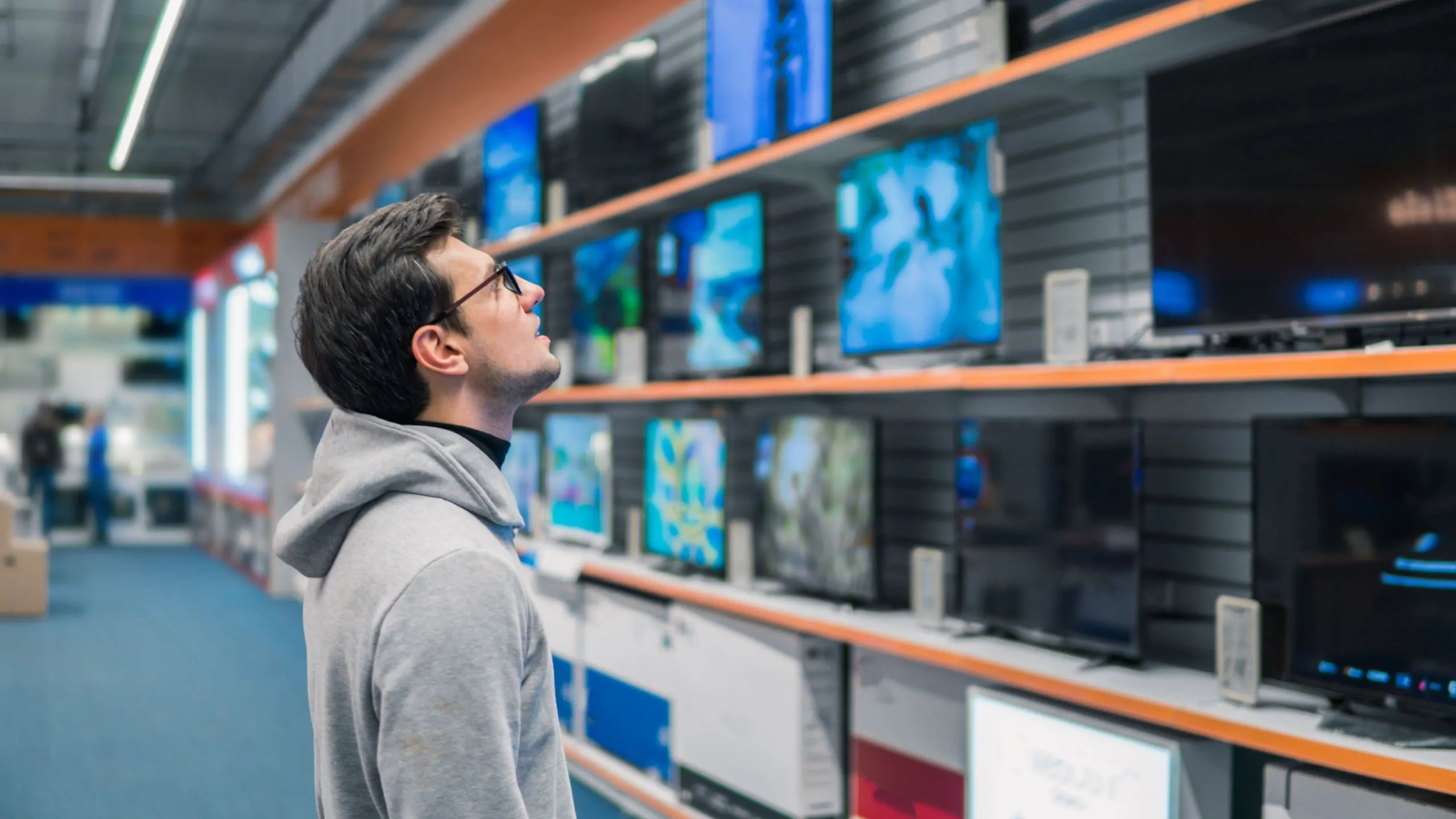 Người đàn ông đang xem xét các mẫu TV thông minh tại cửa hàng điện tử để đưa ra lựa chọn phù hợp.
