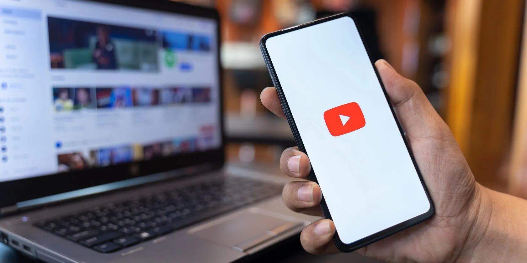 Người dùng đang cầm điện thoại với ứng dụng YouTube và trang web YouTube