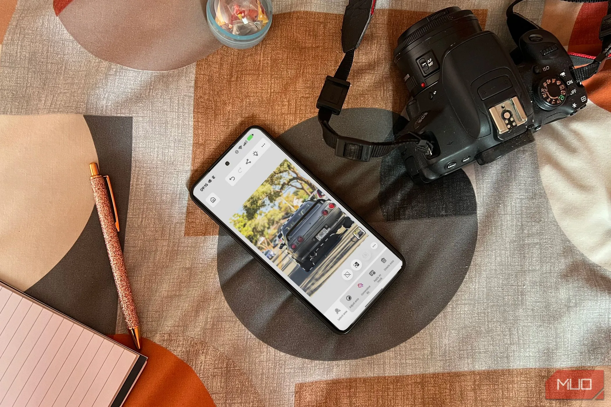 Người dùng đang trải nghiệm Photoshop trên điện thoại Android đặt trên giường cùng máy ảnh và sổ tay