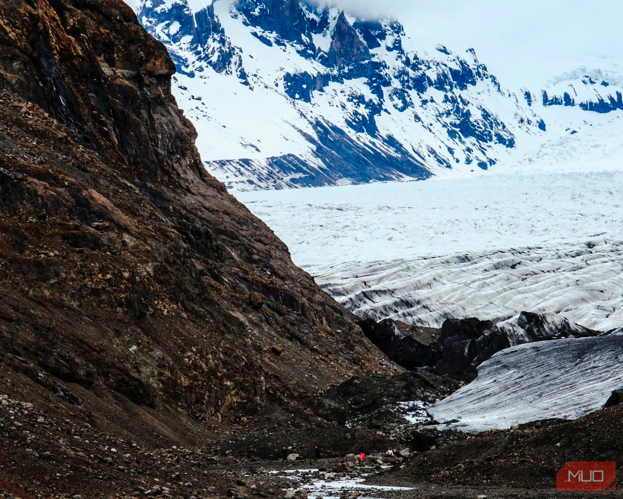Người leo núi mặc áo áo đỏ giữa sông băng và núi non hùng vĩ tại Iceland, cho thấy quy mô cảnh quan.