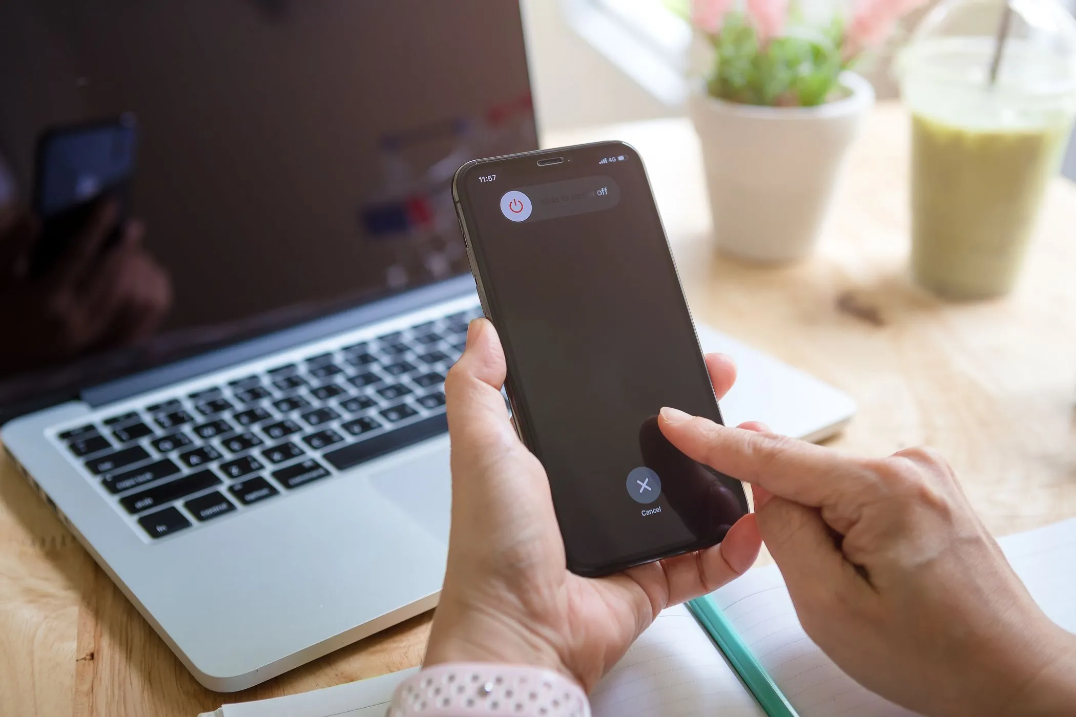 Người phụ nữ đang tắt iPhone gần MacBook, minh họa cho lầm tưởng về việc tắt nguồn để sạc nhanh hơn.