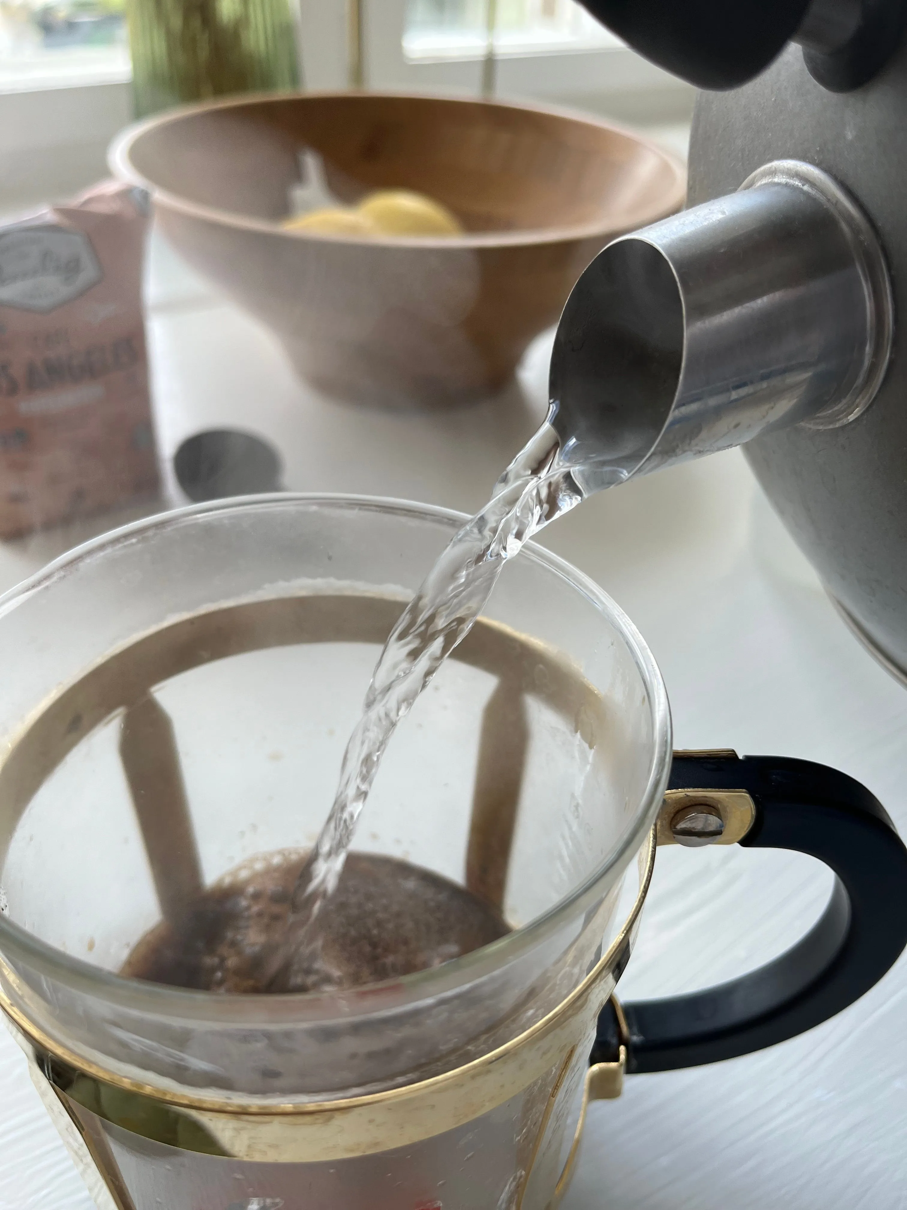 Nước nóng đang được rót từ ấm đun siêu tốc vào bình pha cà phê, ghi lại khoảnh khắc chuẩn bị đồ uống hàng ngày.