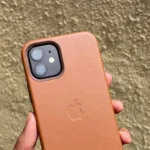 Ốp lưng da màu nâu be cho iPhone 12 được một bàn tay cầm, làm nổi bật chất liệu da cao cấp và khả năng lên "patina" theo thời gian.