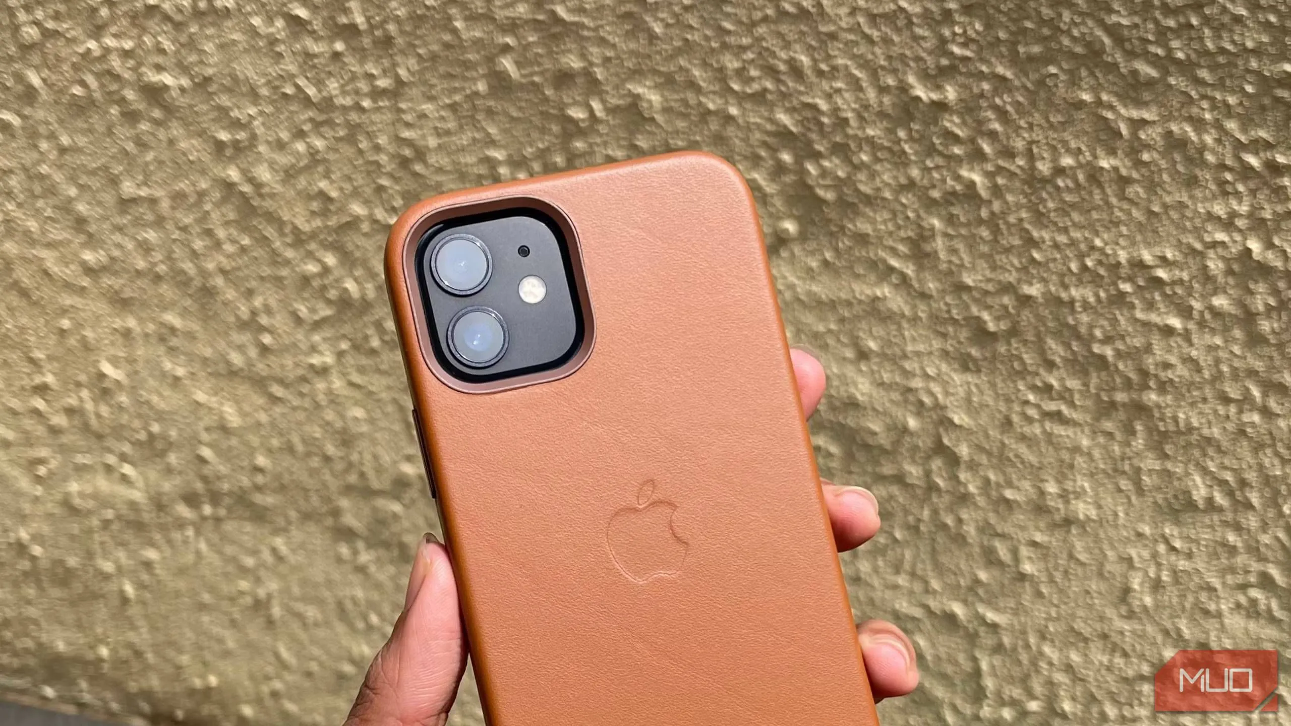 Ốp lưng da màu nâu be cho iPhone 12 được một bàn tay cầm, làm nổi bật chất liệu da cao cấp và khả năng lên "patina" theo thời gian.